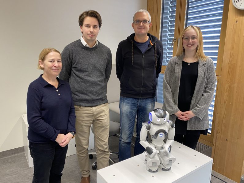 Four researchers standing behind a robot inside a room 