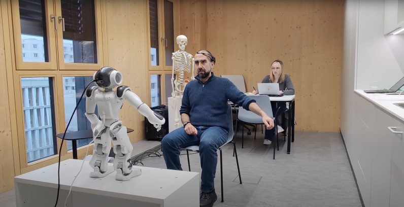 Two researchers trialing a robot's ability to mimic arms movements inside a room 