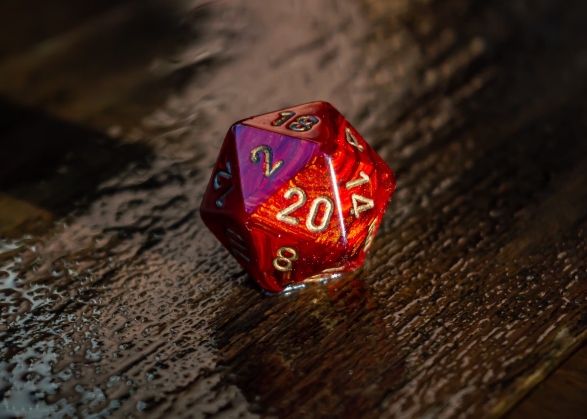 Close-up image of a marbled red 20 sided die on a wet wooden surface outside in the sunlight.
